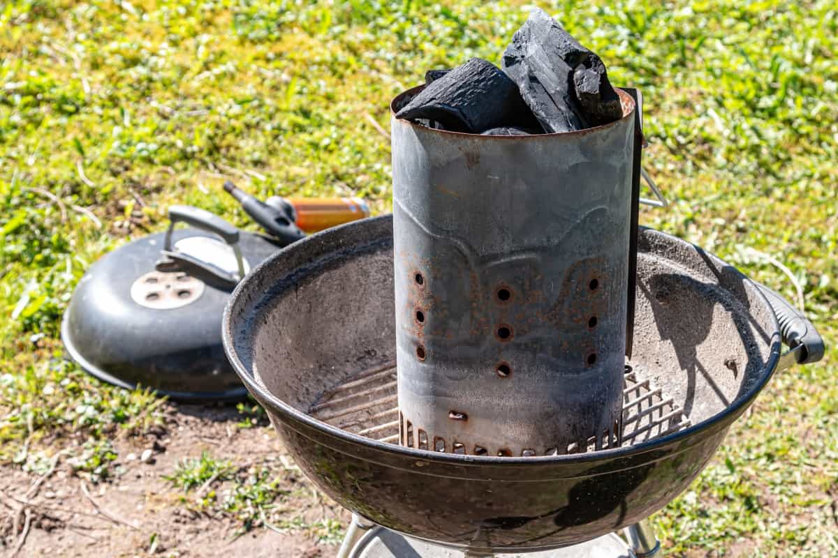 A charcoal chimney starter full of lumpwood charcoal in a kettle grill