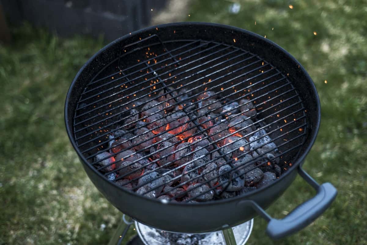 A kettle grill with charcoal spread out in base that's barely lit