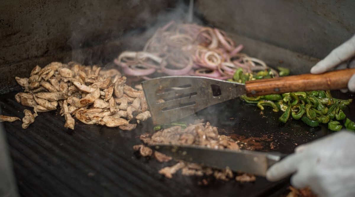 Small meats and vegetables being grilled on a grill mat.