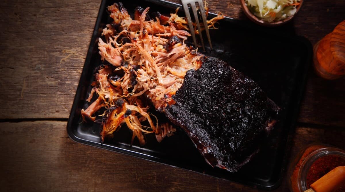 Overhead shot of pulled pork being shredded with forks.