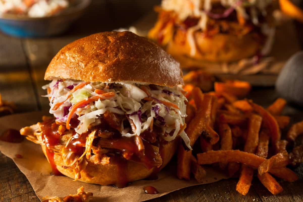 A pulled pork roll next to some French fries on parchment paper