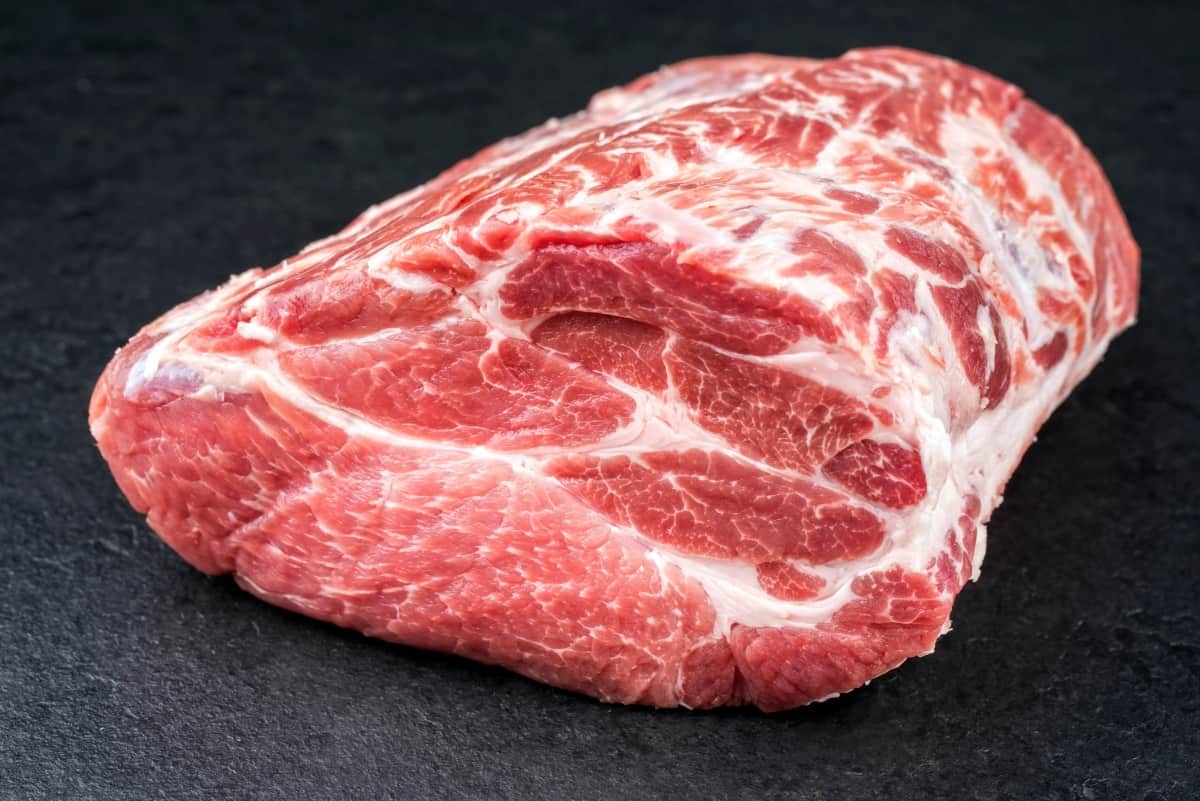 A raw pork Boston butt on a dark surface