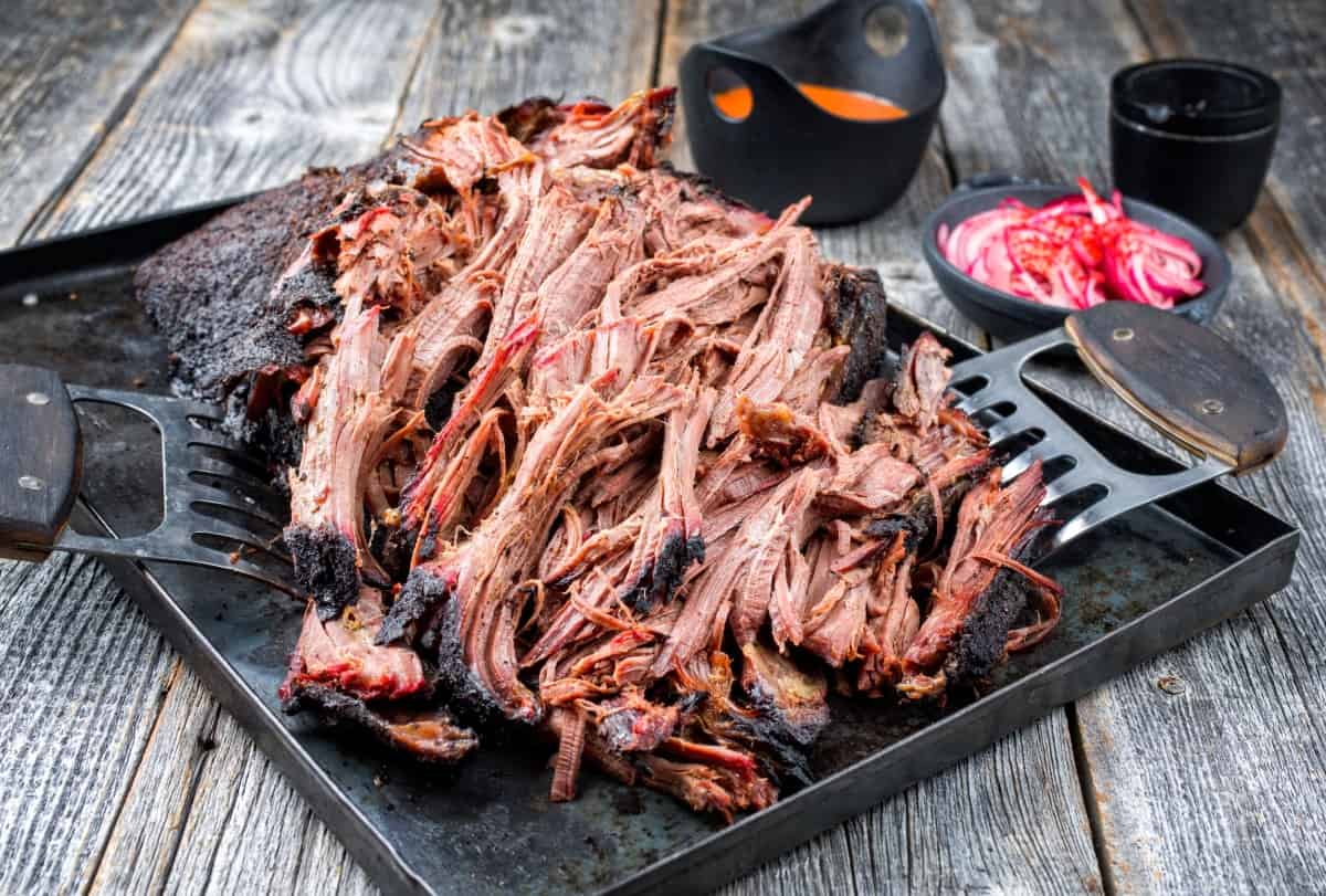 shredded pulled pork on a dark platter, with two meat claws