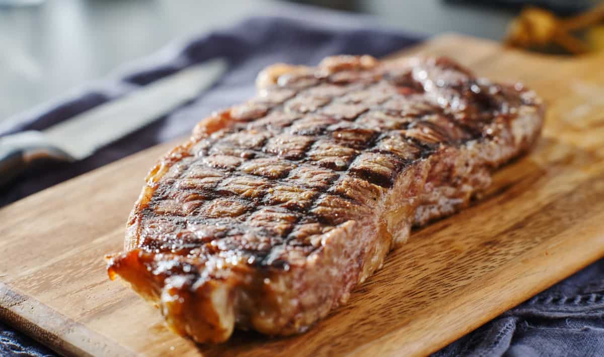 A grilled NY Strip steak resting on a cutting bo.