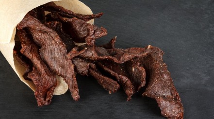 A paper roll full of beef jerky on a dark background.