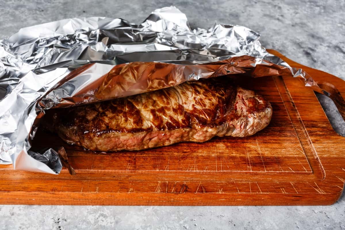 A steak resting under foil on a cutting bo.