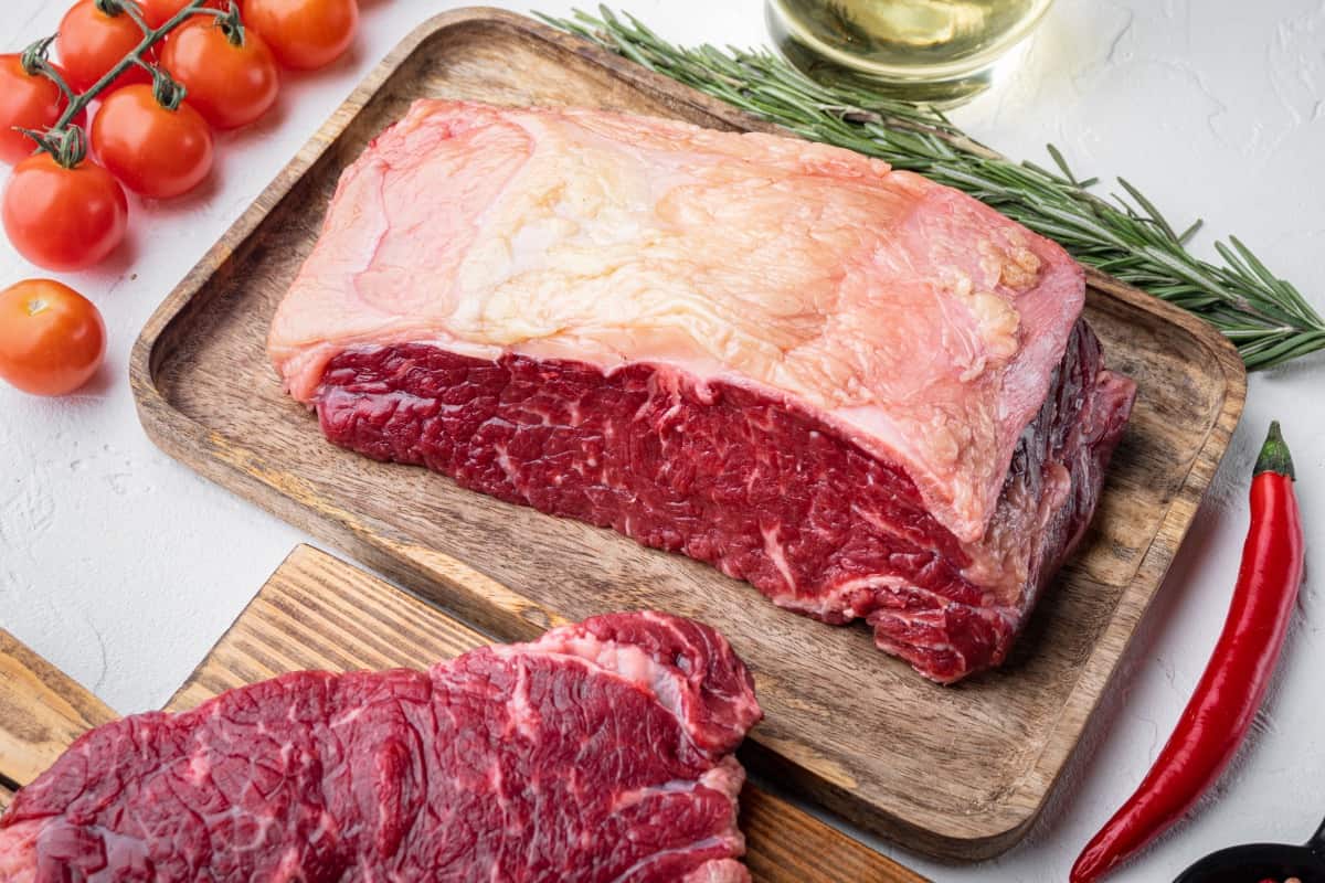 Large piece of raw short loin on cutting board with a steak sliced off