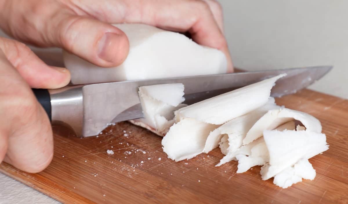 A man's hands slicing beef tallow with a boning kn.