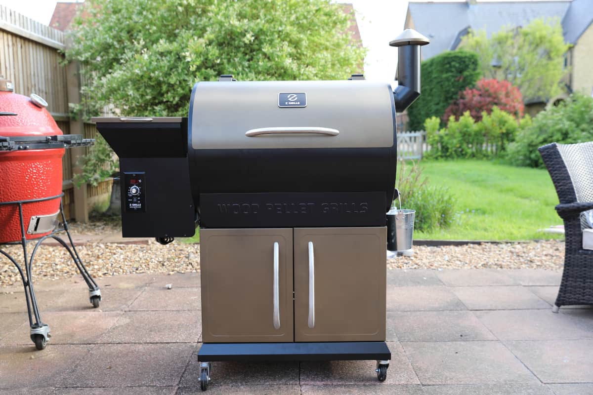 The Z Grills 700D pellet grill sitting on a patio next to a kamado gr.