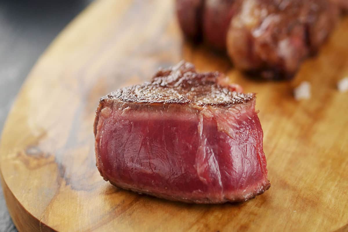 A small cube of blue rare grilled steak on a round cutting bo.