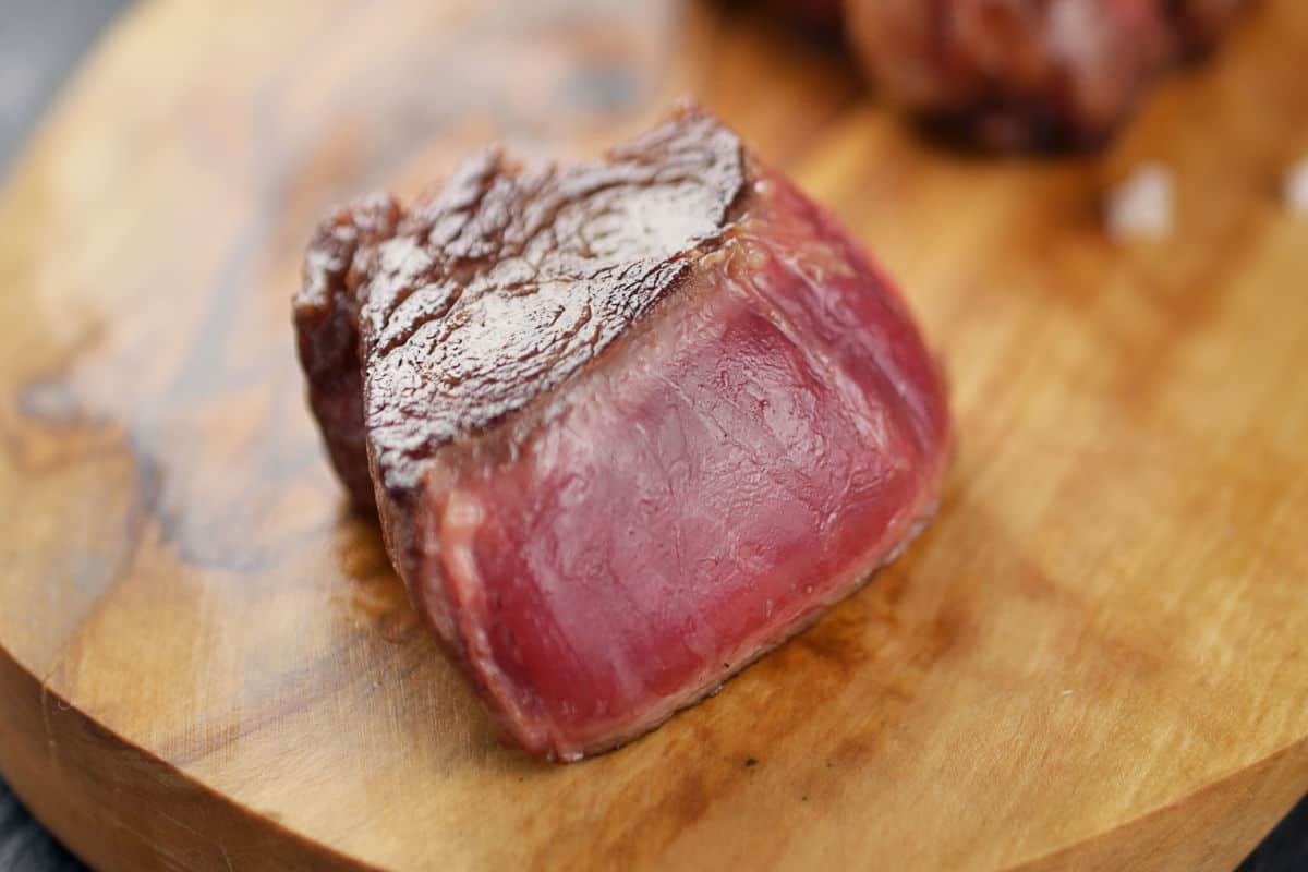 A cube of blue rare grilled steak on a wooden bo.