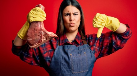 A woman in yellow gloves holding a gone bad steak, making a thumbs down gesture