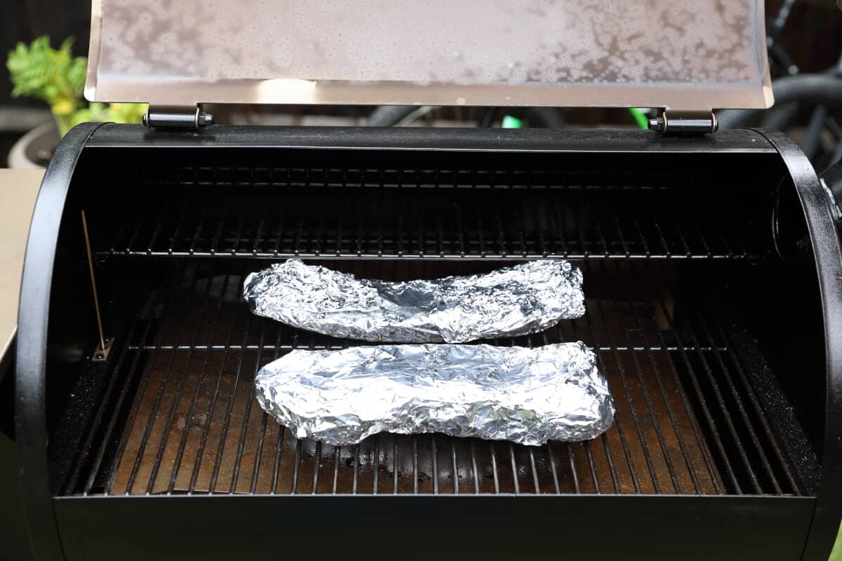 Ribs wrapped in foil on a pellet grills grates.