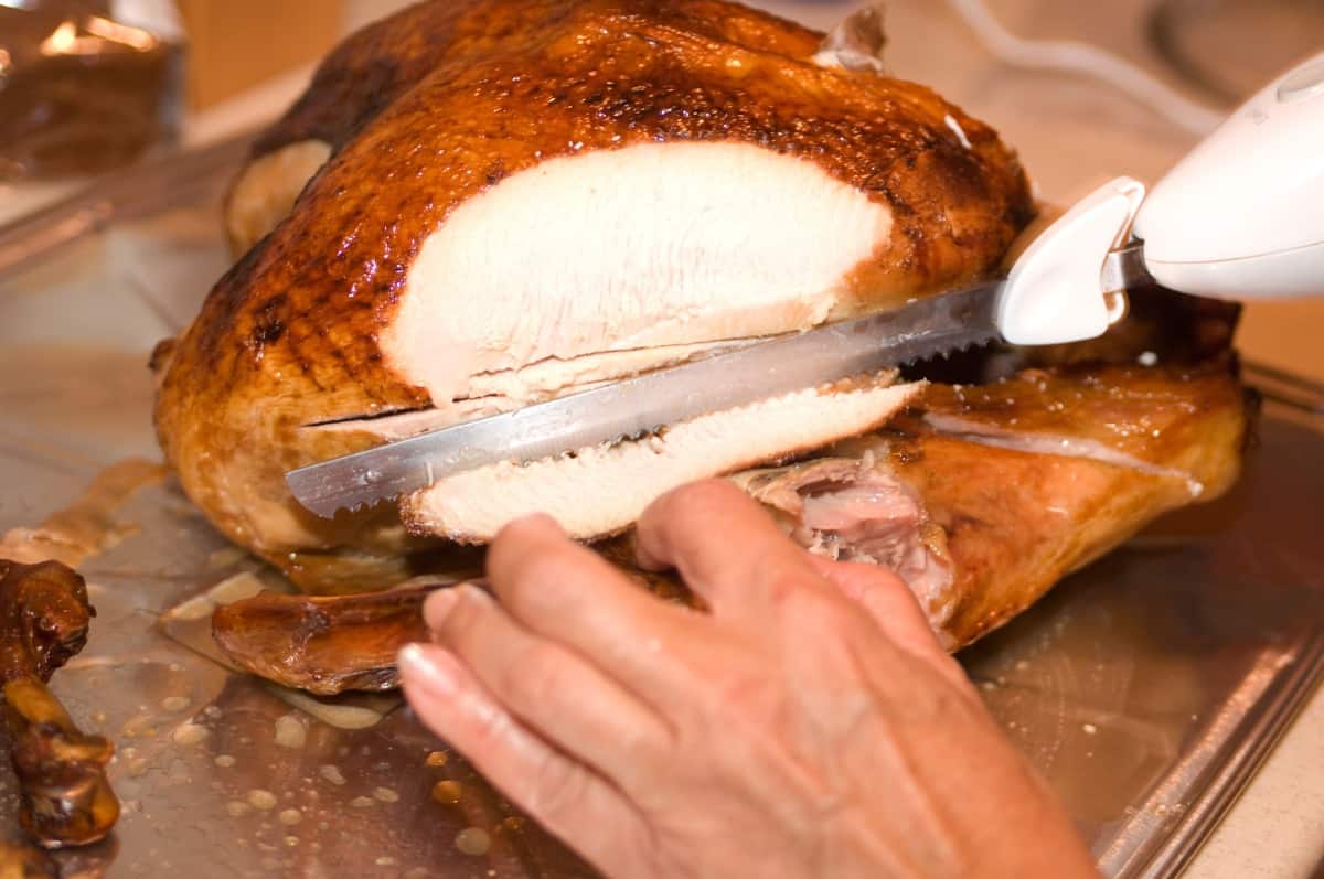 A turkey being carved by male hands on a cutting bo.