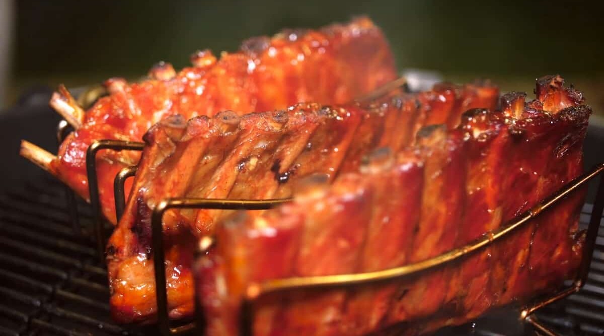 Three racks of ribs in a rack, being smoked in a charcoal smoker.