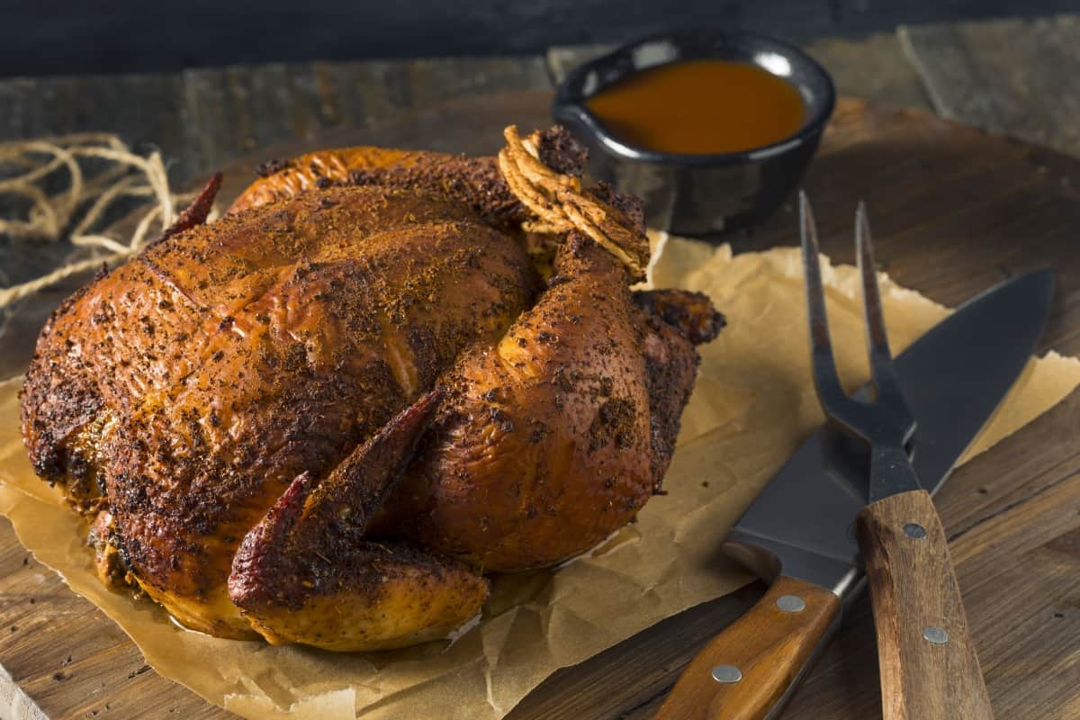 A smoked rubbed chicken on a cutting board about to be car.