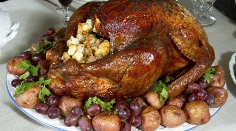Whole smoked turkey with potatoes and grapes on a serving plate