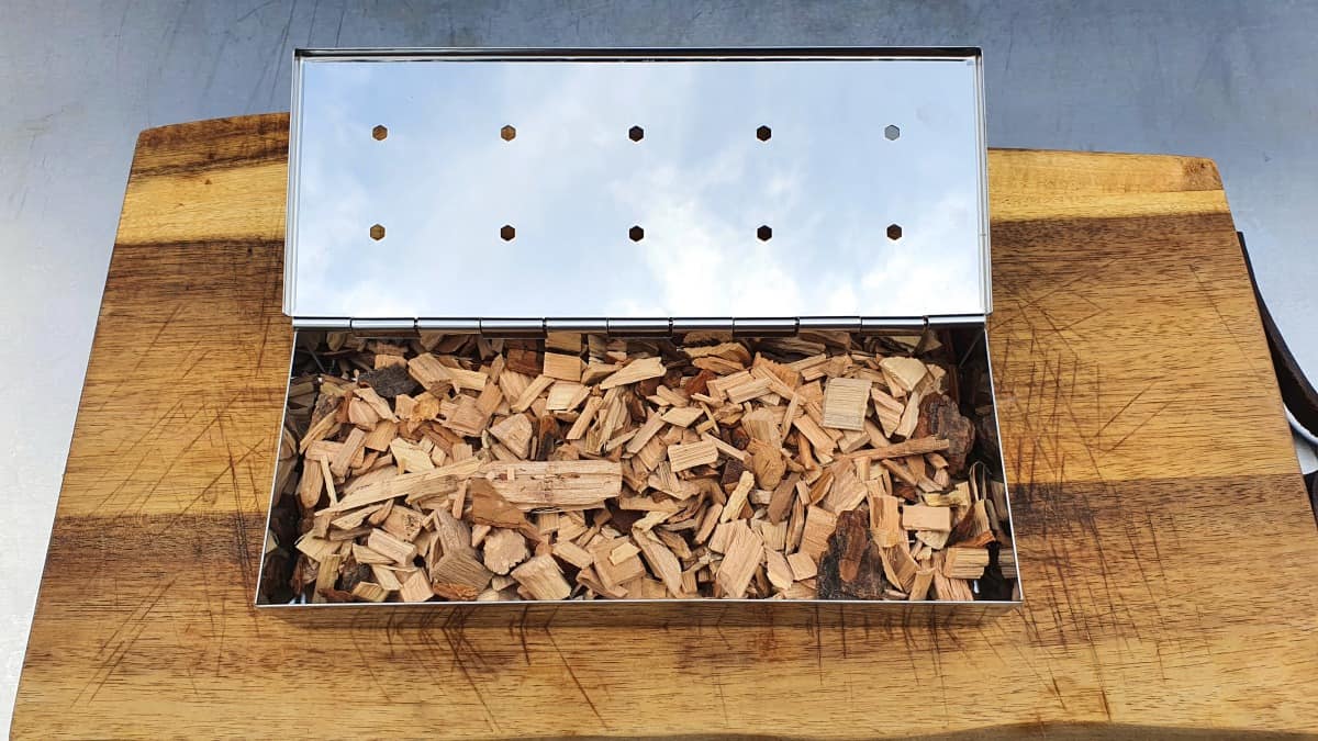 smoker box filled with wood chips, sitting on a cutting bo.