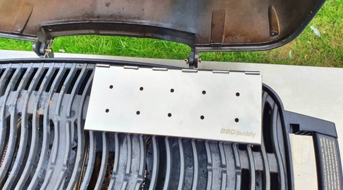 A silver smoker box on the grates of a portable gas grill.