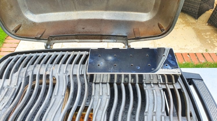 Metal smoker box sitting on the grates of a gas grill.