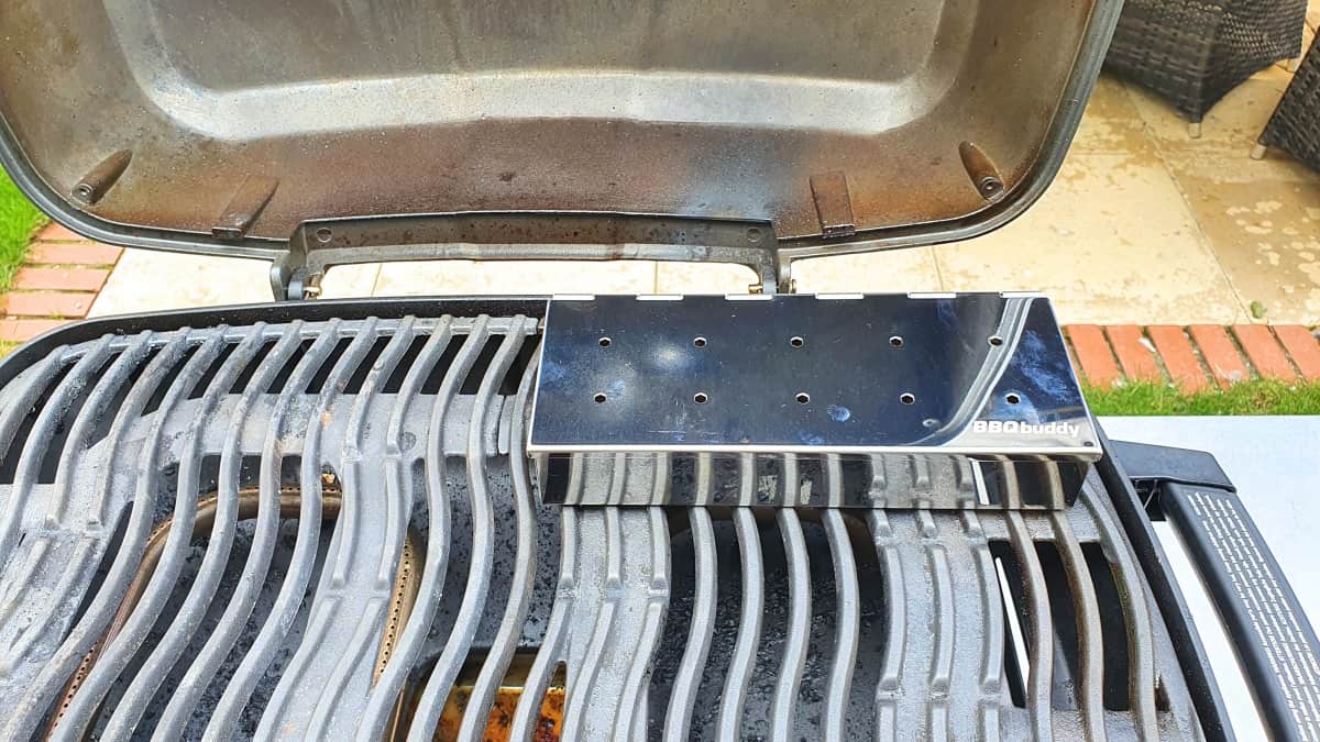 Metal smoker box sitting on the grates of a gas grill