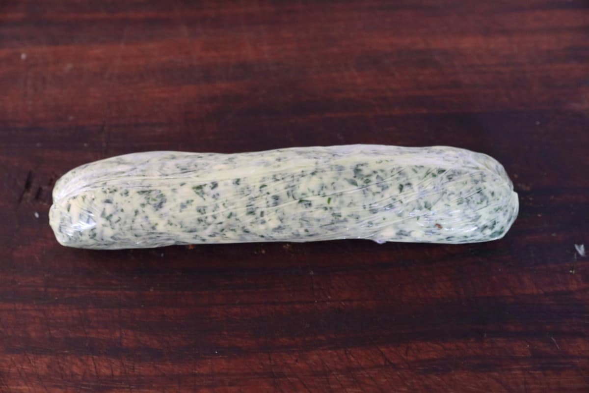 wild garlic butter log wrapped in cling film on a cutting bo.