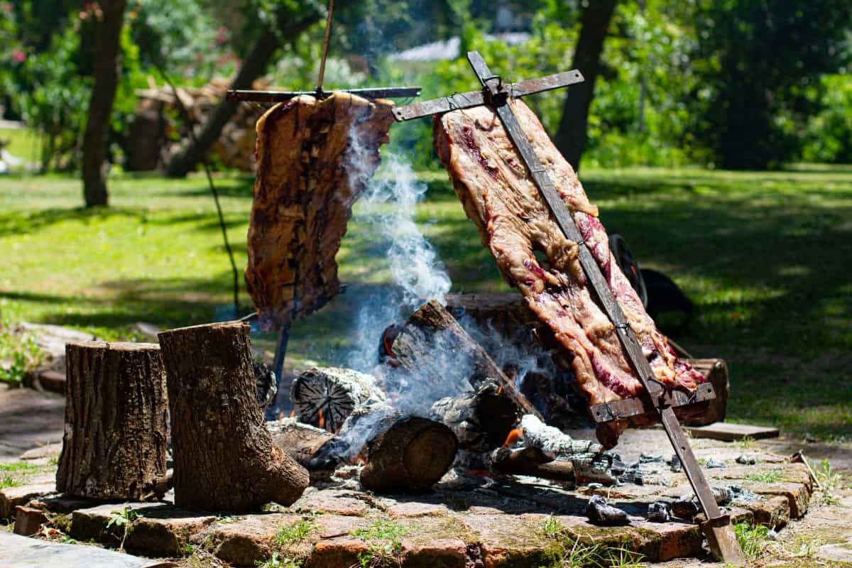 Grilling two lambs on crosses beside an open f.