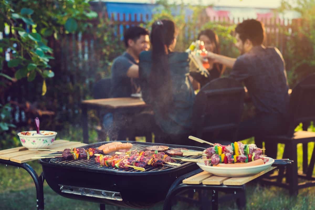 Foods cooking on an open grill, in front of a table of people dining outdo.