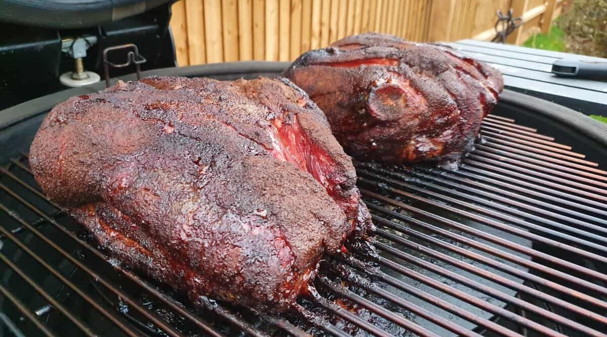 Two large pork butts smoking on a kamado grill.