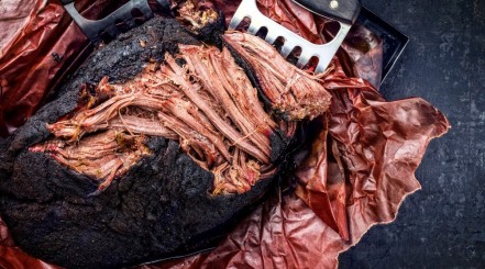 Smoked pork butt on butcher paper with two meat claws, the top part having been pulled and shredded