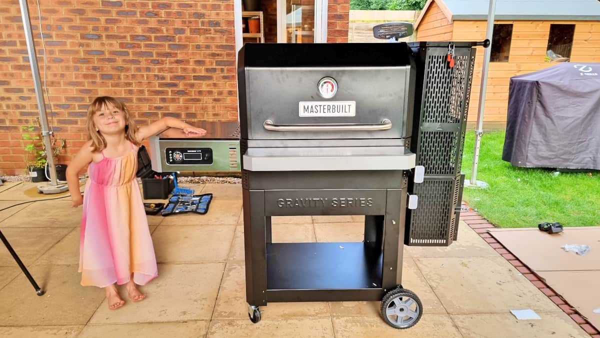 Young girl stood besidede a Masterbuilt gravity fed 1050 smoker