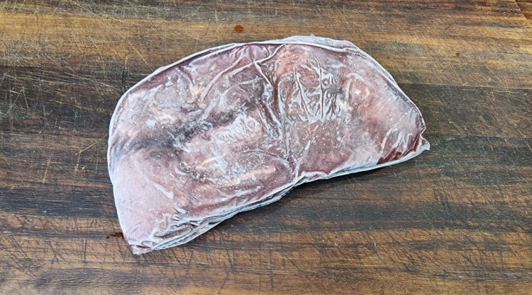 a frozen steak in vac pack, sitting on a wooden cutting board