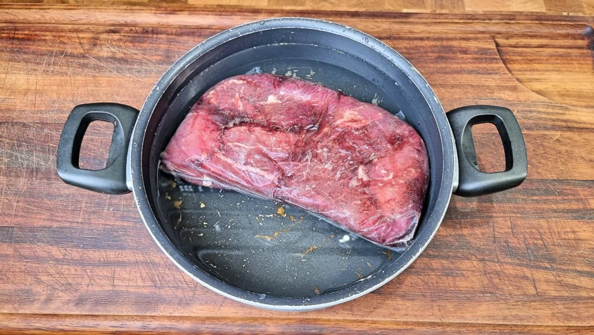 A steak defrosting in a pan of cold water, on a wooden cutting board