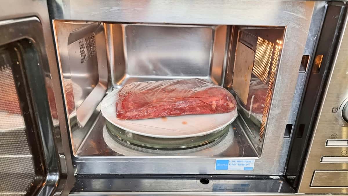 Frozen steak on a plate, in a microwave with the door open