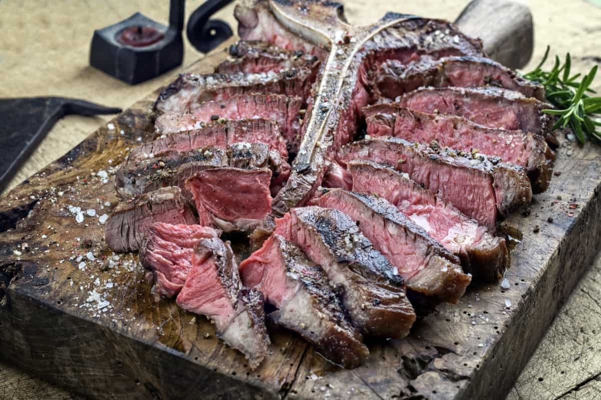 dry-aged porterhouse steak, grilled to medium rare and sliced on a dark wooden surf.