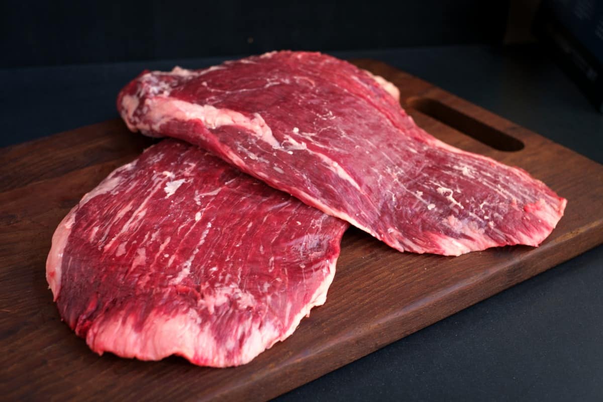Two pieces of raw flank steak on a dark wooden board