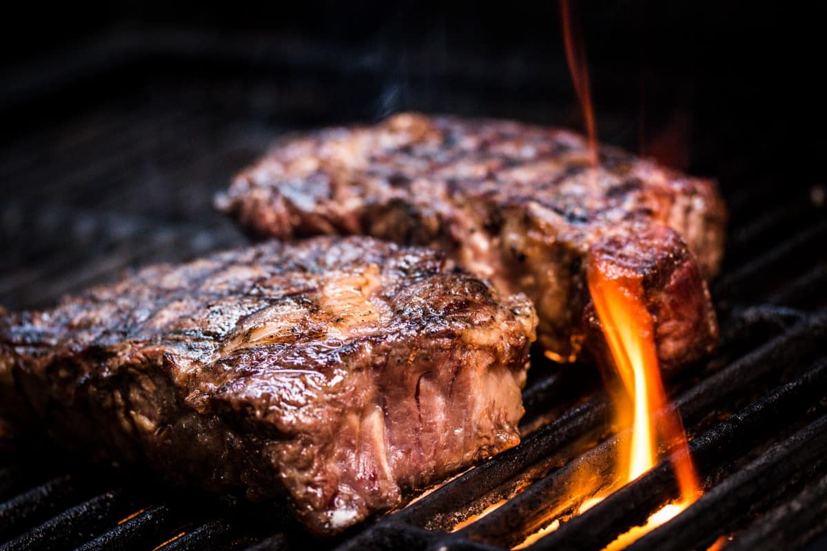 Two thick steaks being grilled over flaming charc.