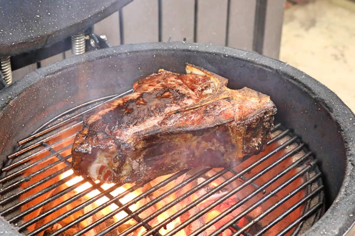 A porterhouse steak being grilled on a flaming hot Kamado Joe Jr. grill