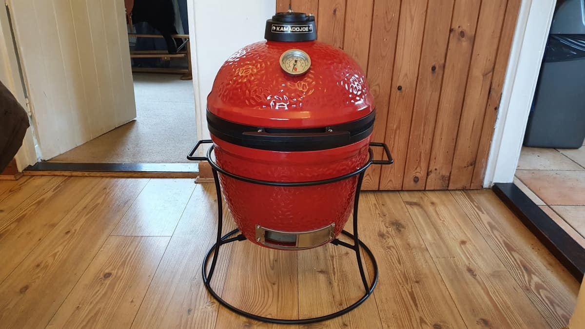 A Kamado Joe jr in its stand, on a wooden fl.