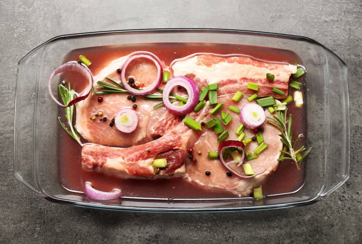 Pieces of meat marinating in a glass bowl, with onions and he.