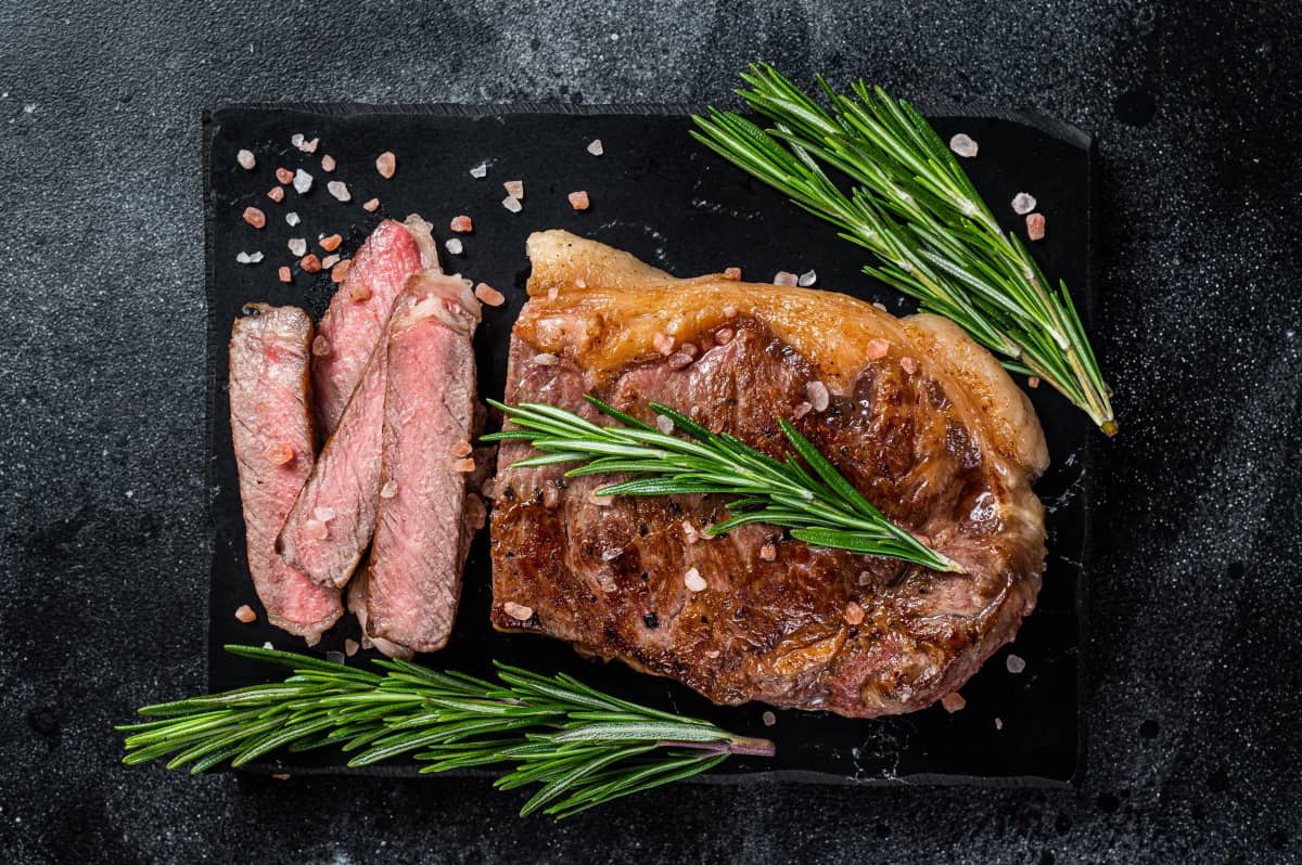 Sirloin steak, grilled to medium-rare, sliced, on a slate board with rosemary spr.