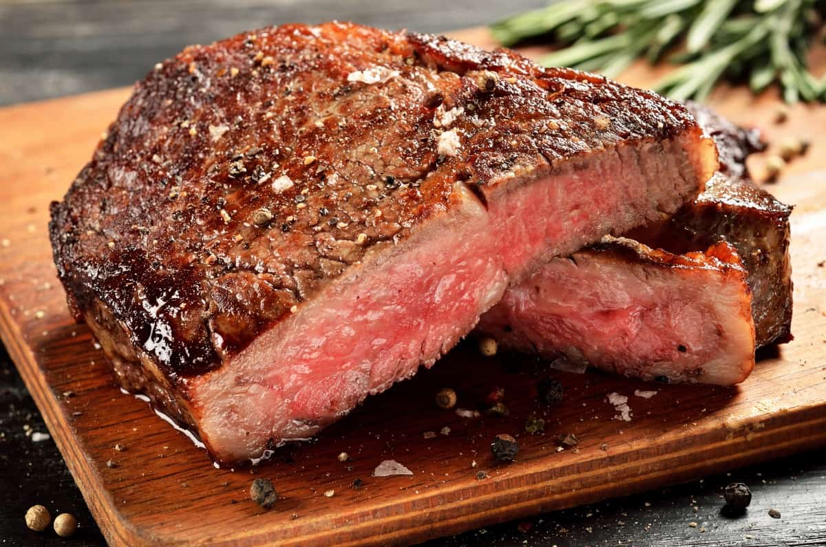 Ribeye steak cooked to medium rare, sliced to see the pink insides, sitting on a wooden cutting bo.