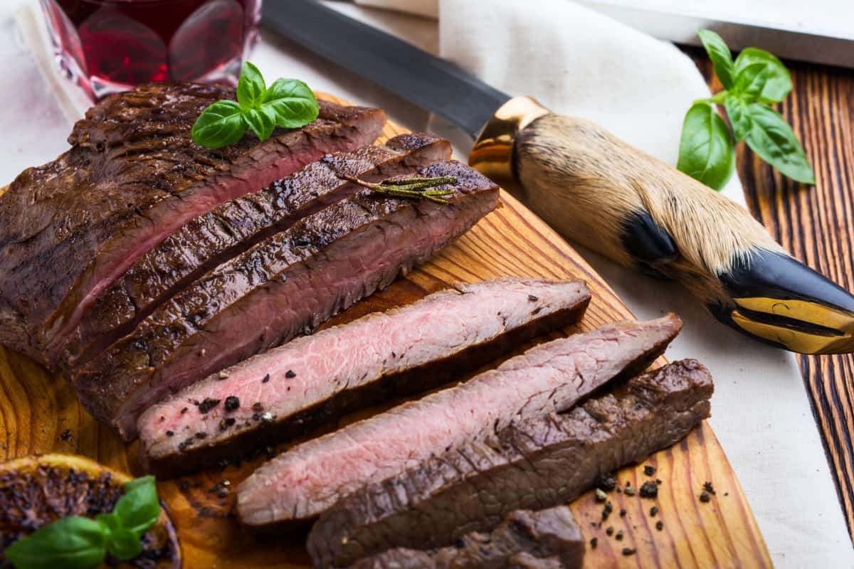 A medium well cooked steak, sliced on a wooden cutting board, with a knife that has a deer foot handle