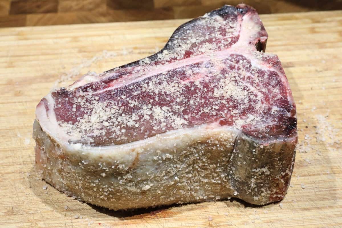 A heavily salted porterhouse steak on a wooden cutting board
