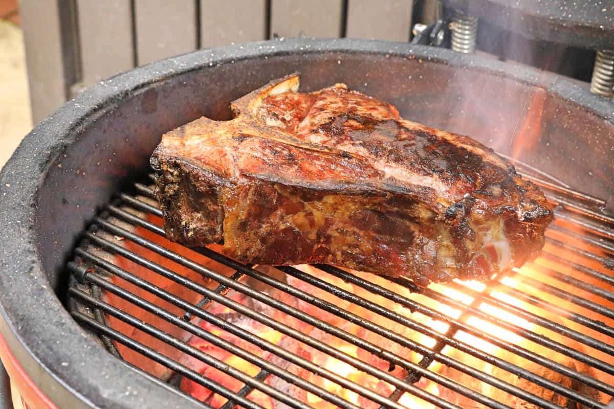 A steak searing over hot flaming charcoal on a Kamado Joe.