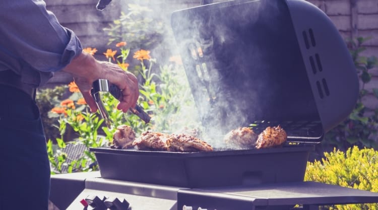 A man turning meat with tongs on a very smoky looking gas grill.