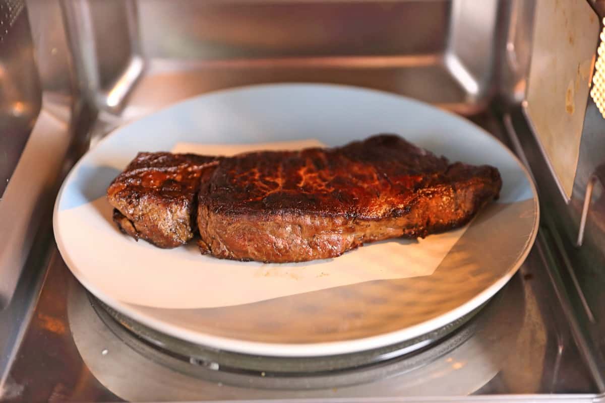 A cooked sirloin steak on a plate in the microwave, about to be rehea.