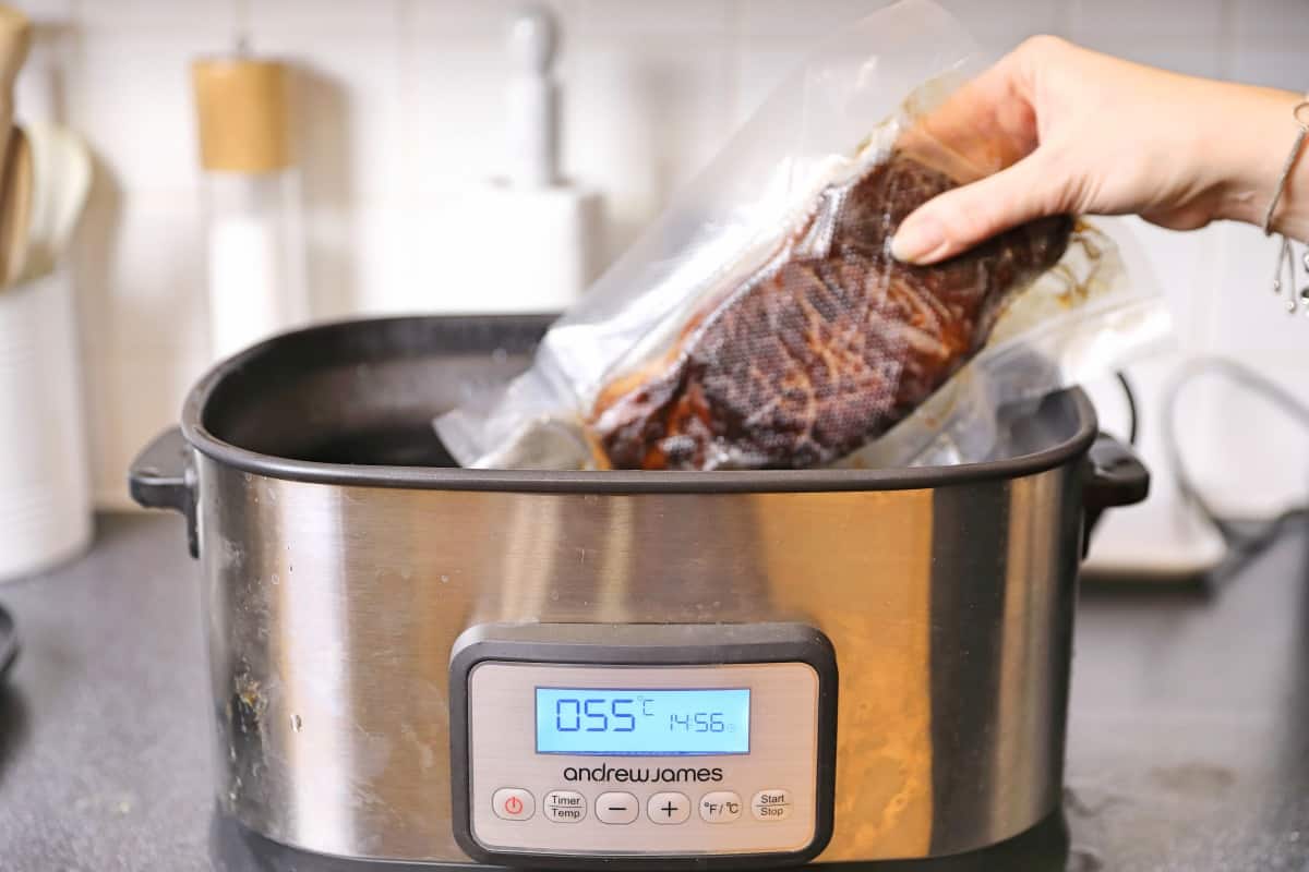 A vacuum packed steak being dropped into a sous vide bath that shows 55 degrees C on it's disp.