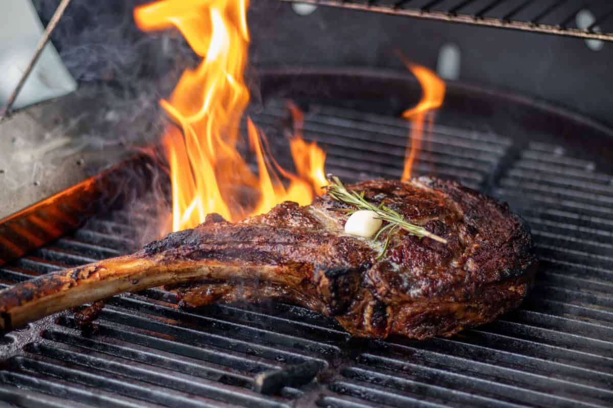A tomahawk steak on a fiery hot grill, with butter and rosemary sprig on .