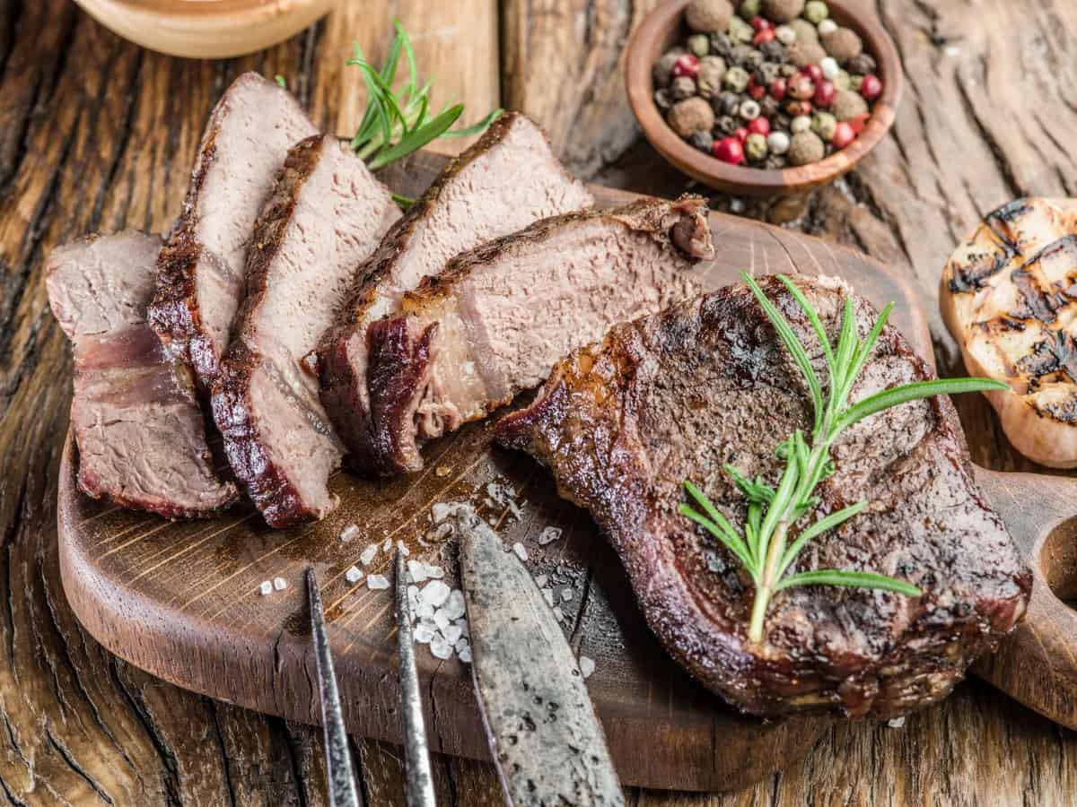 A ribeye steak cooked to well done, sliced on a wooden cutting board, with rock salt and a rosemary sp.